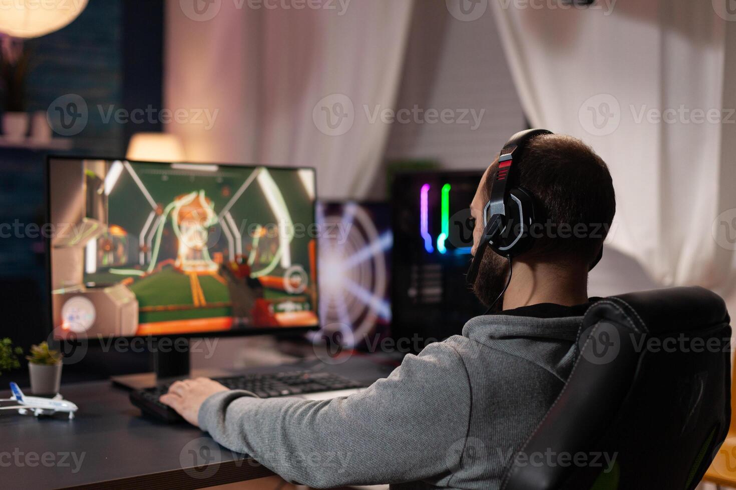 Person using keyboard and mouse to play games on computer. Man wearing headphones and playing online game with mousepad and gaming equipment. Gamer doing activity for entertainment photo
