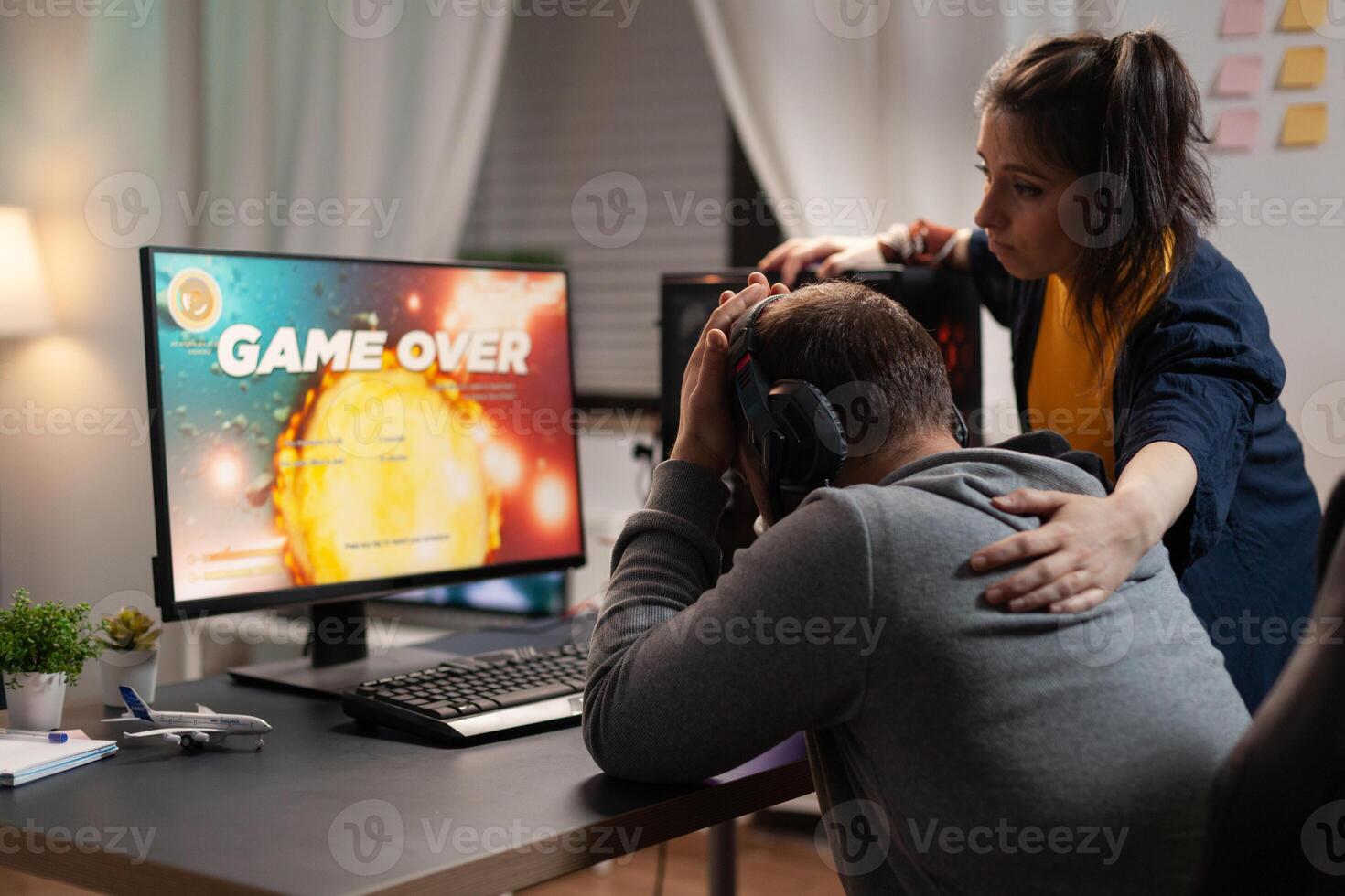Couple feeling sad about losing games play in front of computer. Woman comforting man about lost game online, having gaming equipment and headphones, playing for leisure. photo