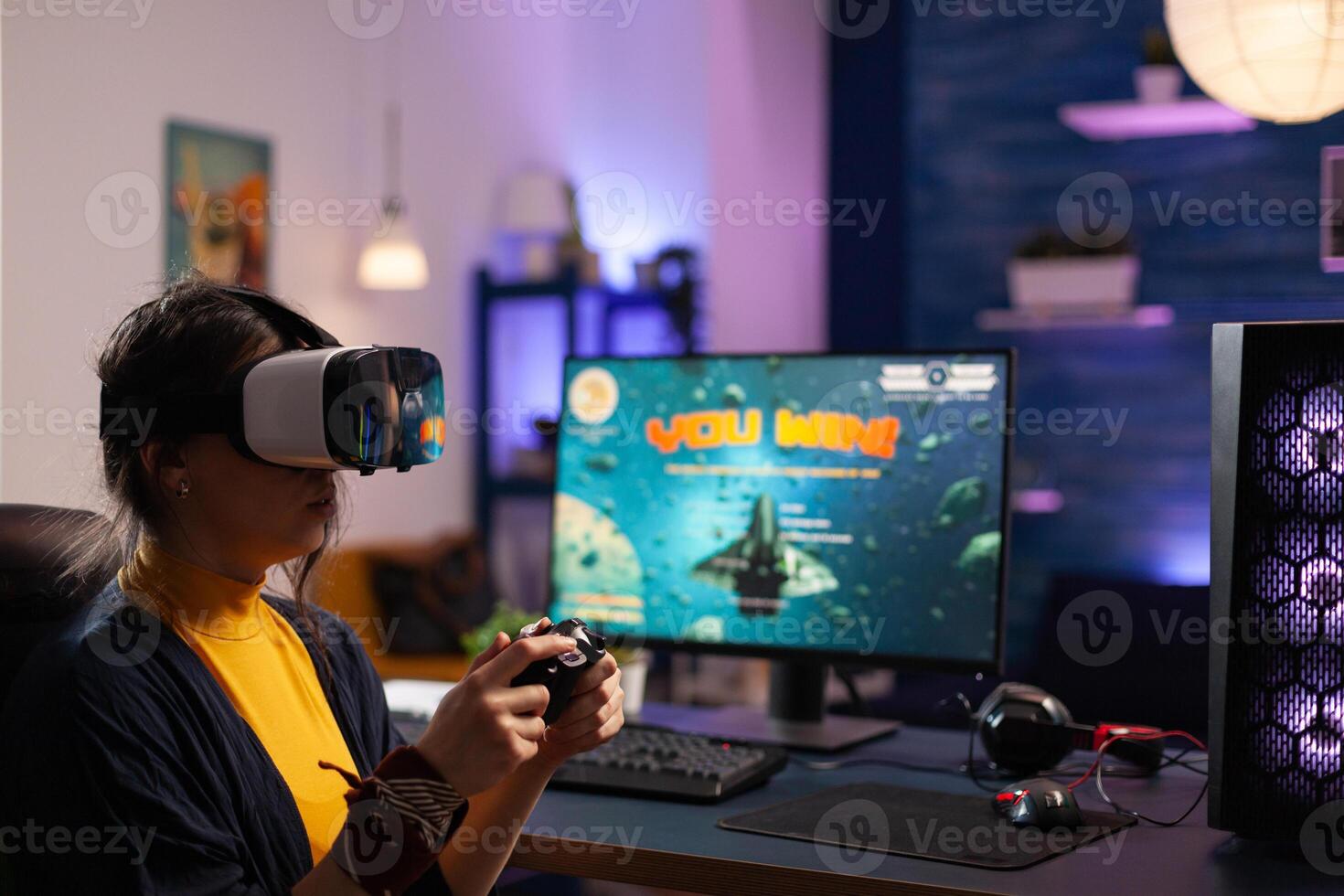 Woman winning games with vr glasses on computer. Gamer playing with virtual reality headset and controller to win online game on monitor. Player with modern equipment at desk. photo