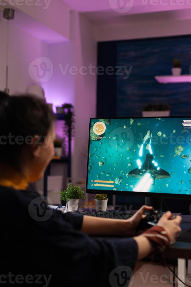 Gamer playing games with joystick on monitor. Cheerful woman using controller to play online game on internet. Player doing fun activity in cyber space with gaming equipment. photo