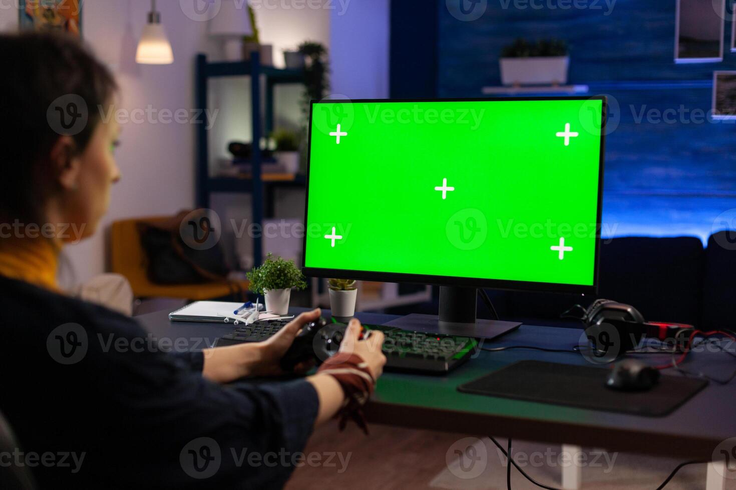 Woman looking at horizontal green screen on monitor, playing games with controller. Gamer using chroma key with isolated background and mockup template on computer display. photo