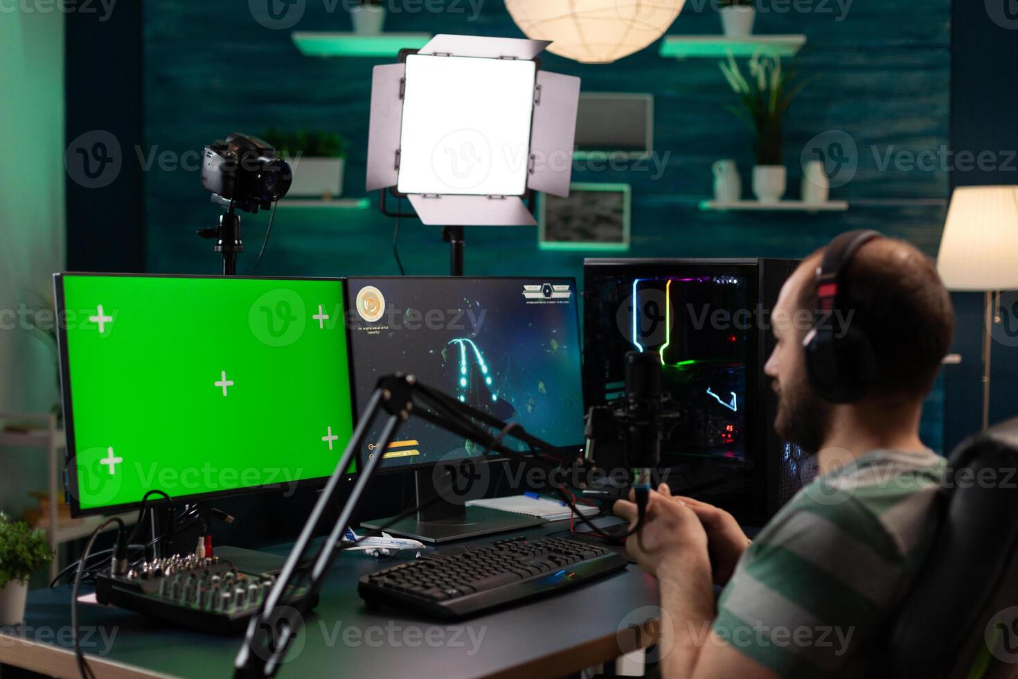 Man streaming games and using horizontal green screen. Person playing online games while he has chroma key with isolated mockup template on computer display. Gamer on stream photo