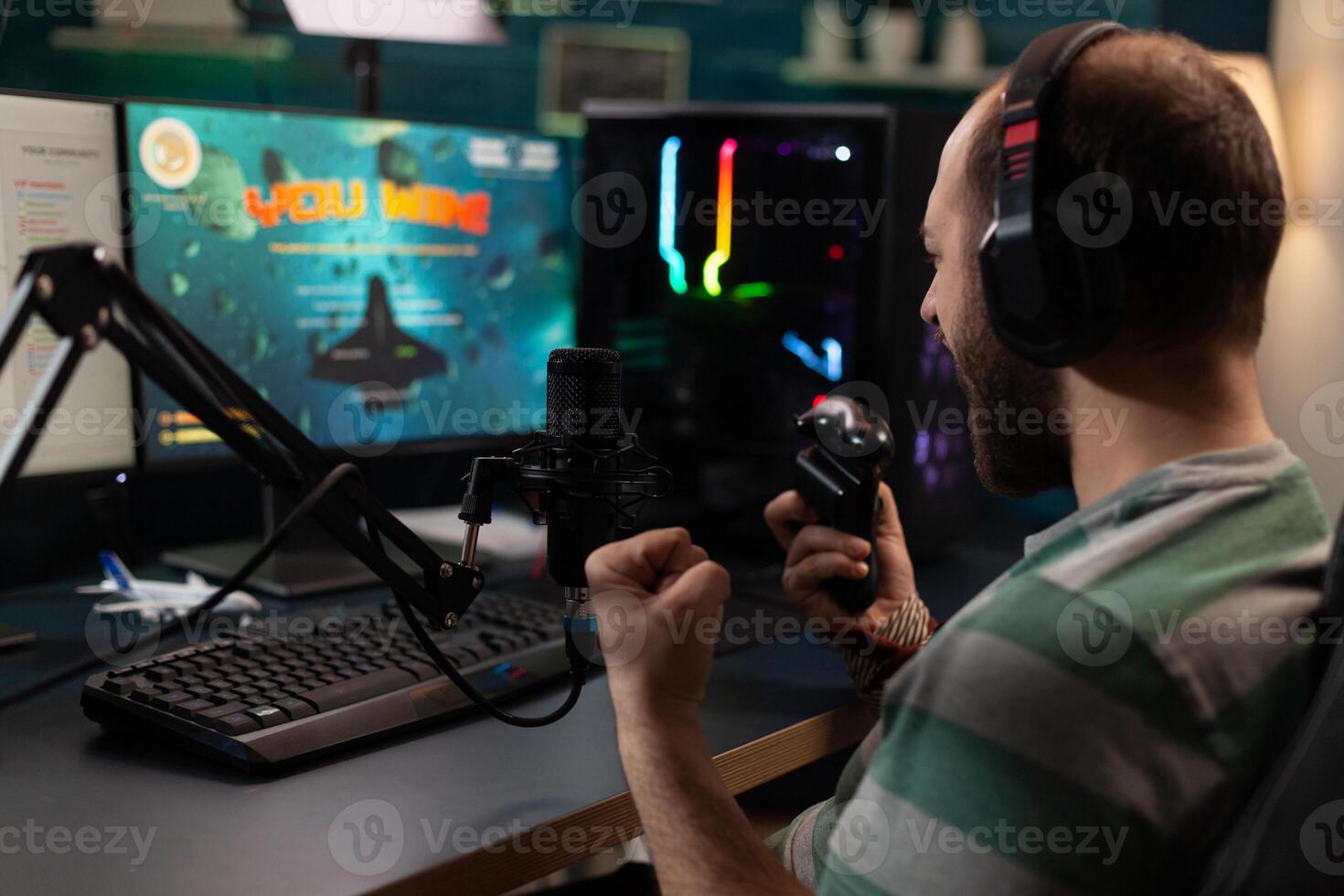 Streamer winning games with joystick on computer. Man live streaming gameplay and celebrating win, using microphone and headphones while he talks to online chat on monitor. Gamer on stream photo