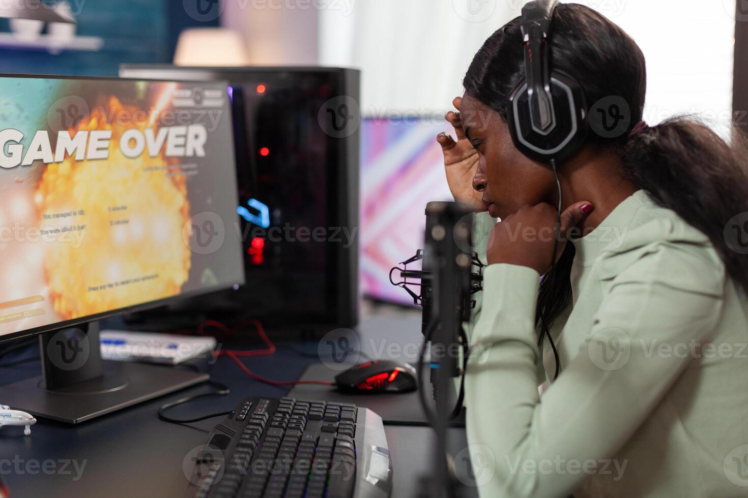 Sad upset woman gamer playing space shooter videogames losing online tournament while talking with players on streaming chat. Nervous streamer using RGB gaming computer. Game over on screen photo