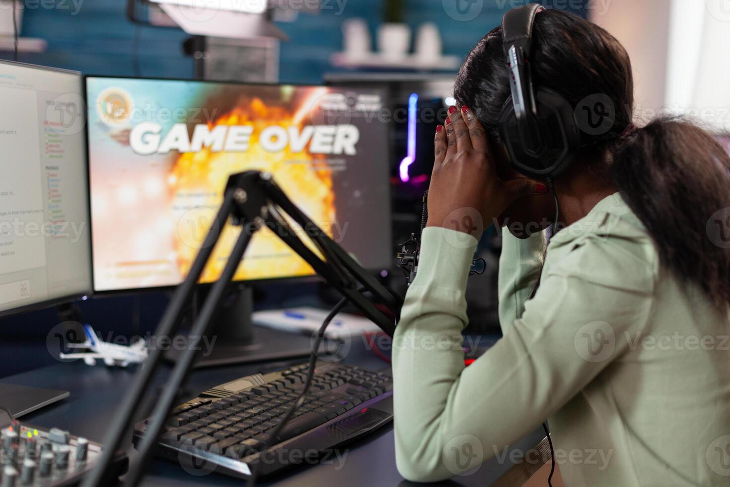 Sad upset pro gamer woman playing space shooter games losing online championship while talking with players on streaming chat. Nervous streamer using RGB gaming computer. Game over on screen photo