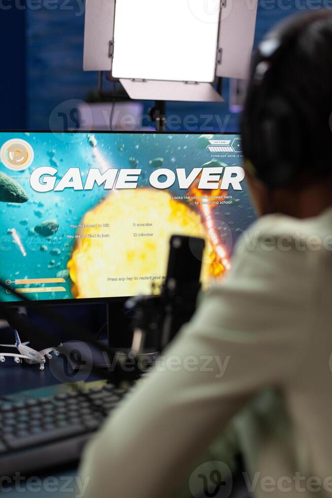 Sad upset esport gamer sitting at gaming desk playing space shooter videogames losing online games championship. Nervous woman streaming live using RGB computer equipment, Game over on screen photo