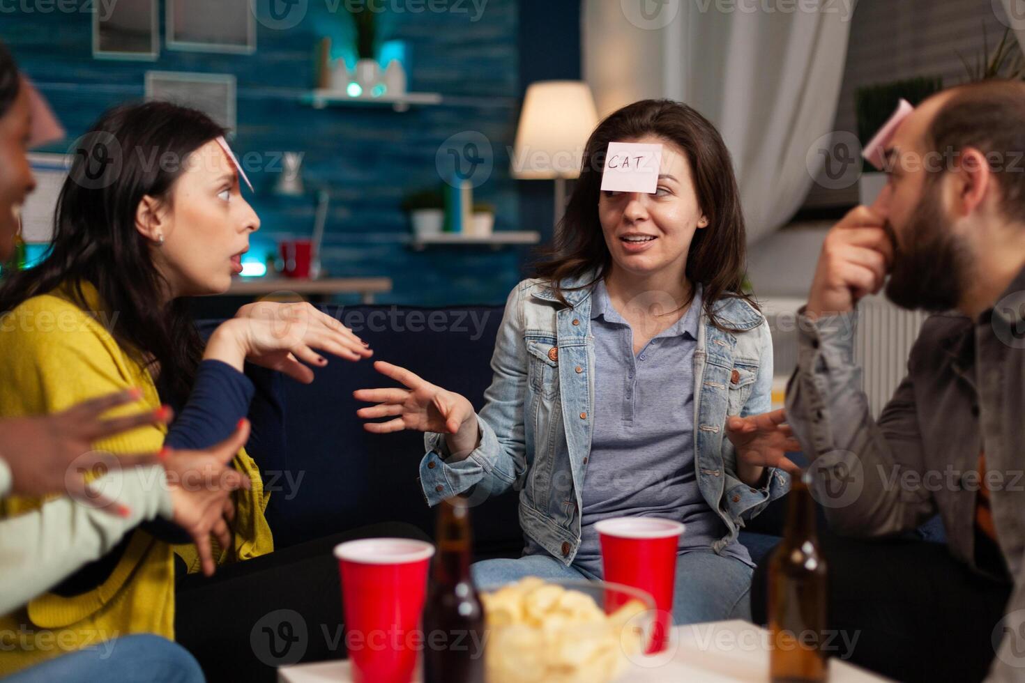Portrait of happy woman with stickey notes on forehead playing guess who game enjoying spending time with friends socializing together during wekeend party at home. Friendship concept photo