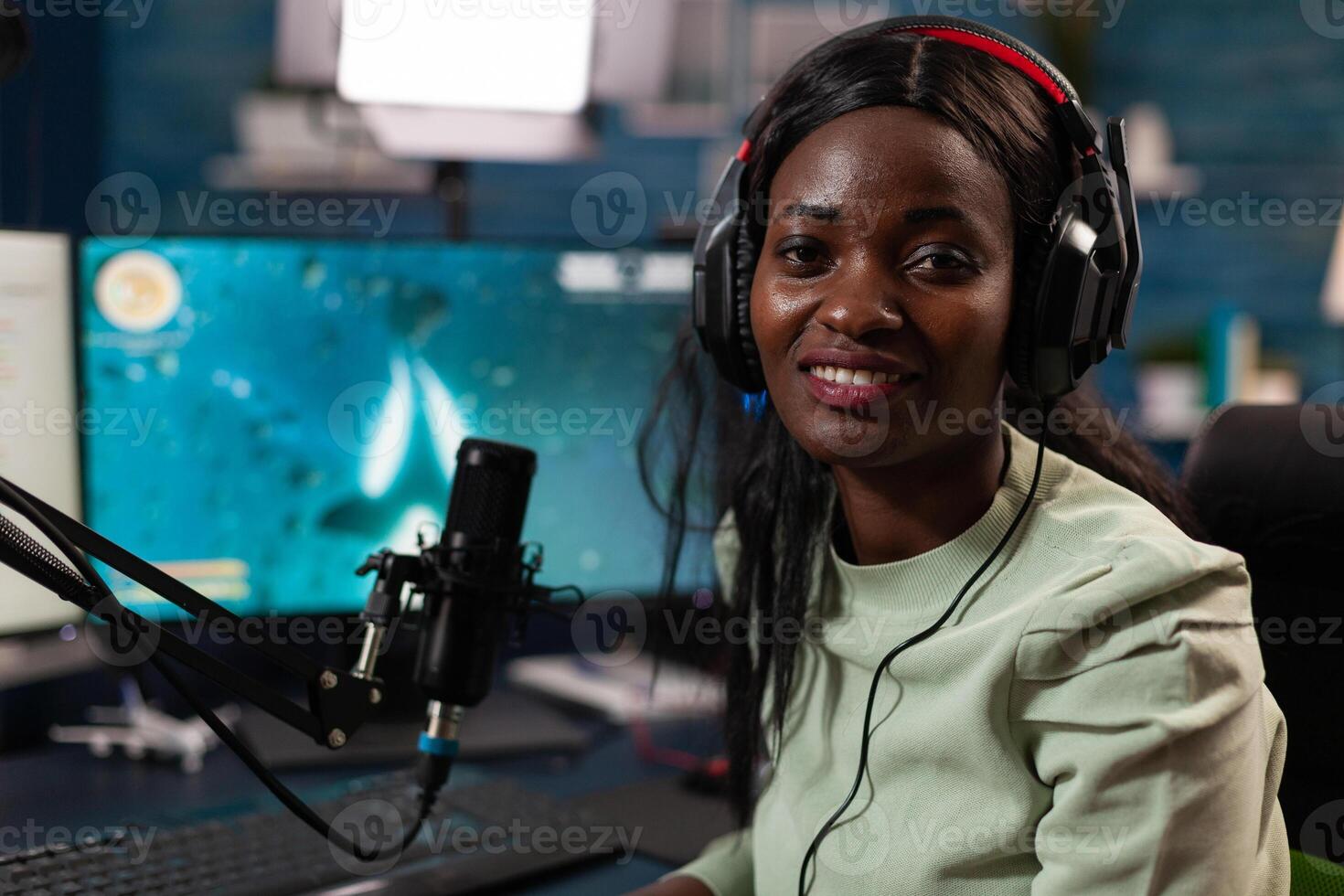 Portrait of african american player smiling at camera while playing space shooter videogame during online championship. Cyber player talking at microphone for streaming live using RGB computer photo