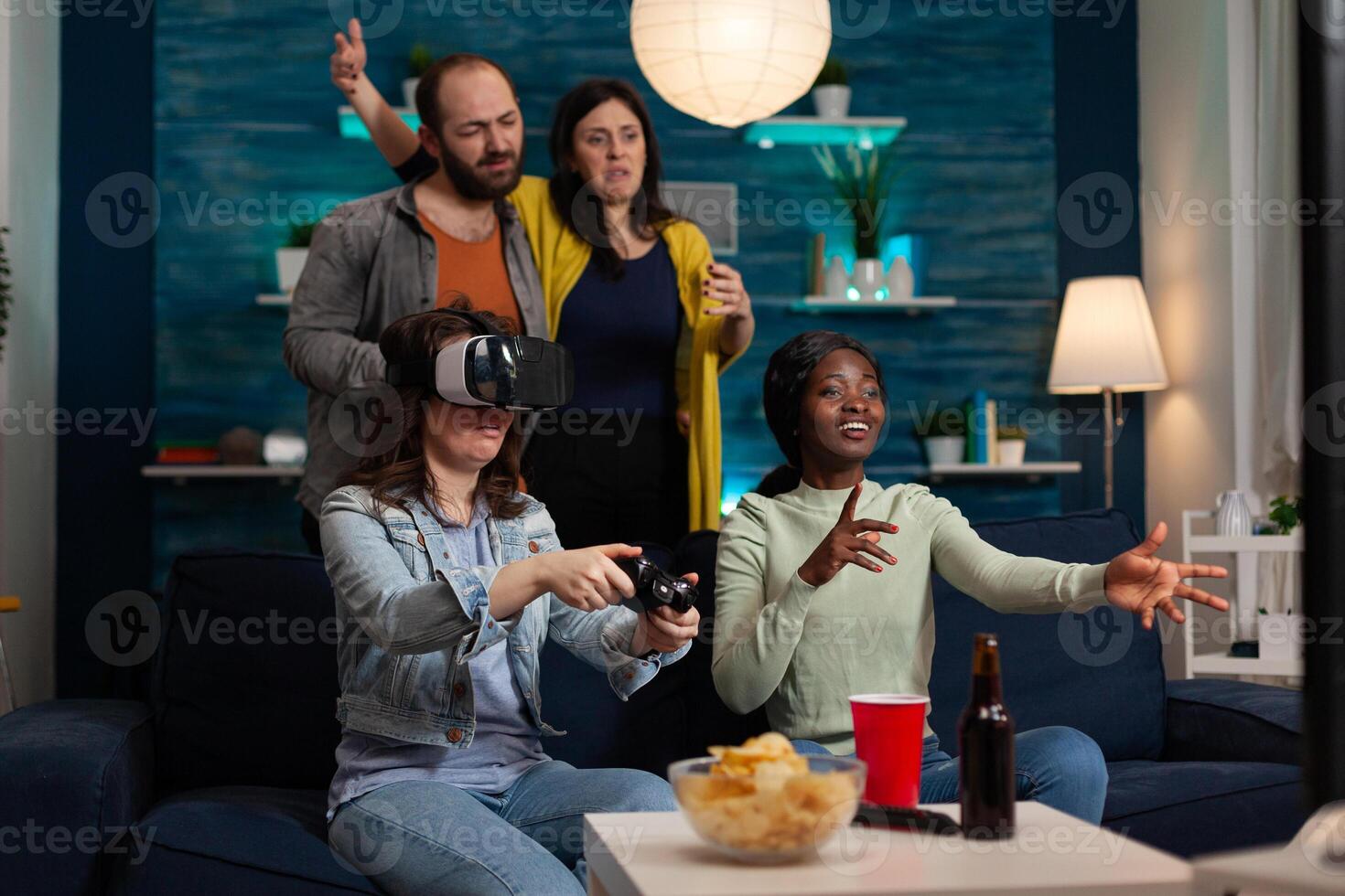 Gamer woman wearing virtual reality headset holding gaming controller playing videogames losing online competition. Group of multi-ethnic friends enjoying hanging out together making fun activity photo