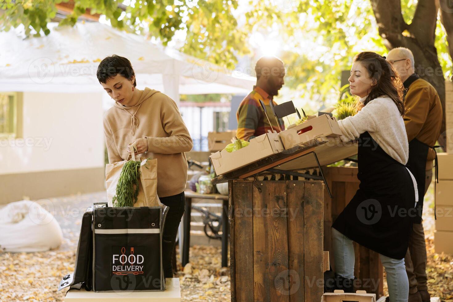 Courier putting package of organic fruits and vegetables delivery. in thermal food bag while standing near market counter, picking up order. Farmers deliver fresh produce to local customers photo