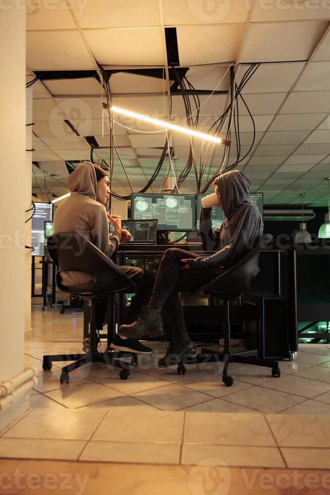 Young hackers coding trojan virus program to hack system, IT specialists programming illegal firewall encryption. Two cybercriminals developing malicious software late at night. photo