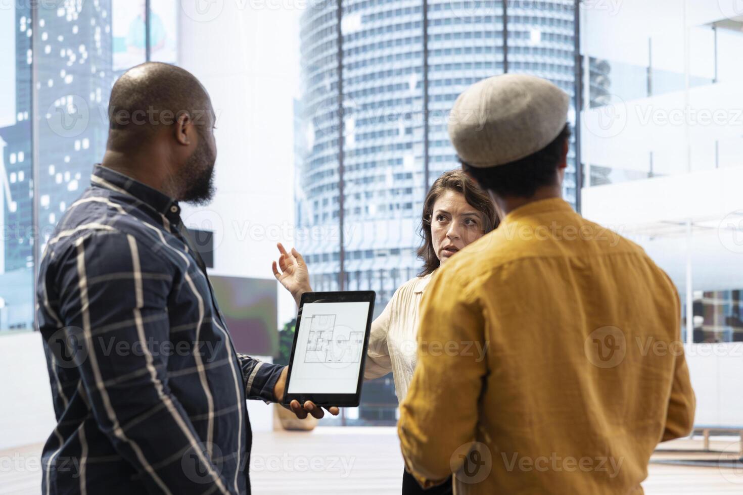 Real estate broker presenting a new high class office space to clients, discussing the detailed blueprints using a tablet during the office tour. Planning an investment strategy involving property. photo