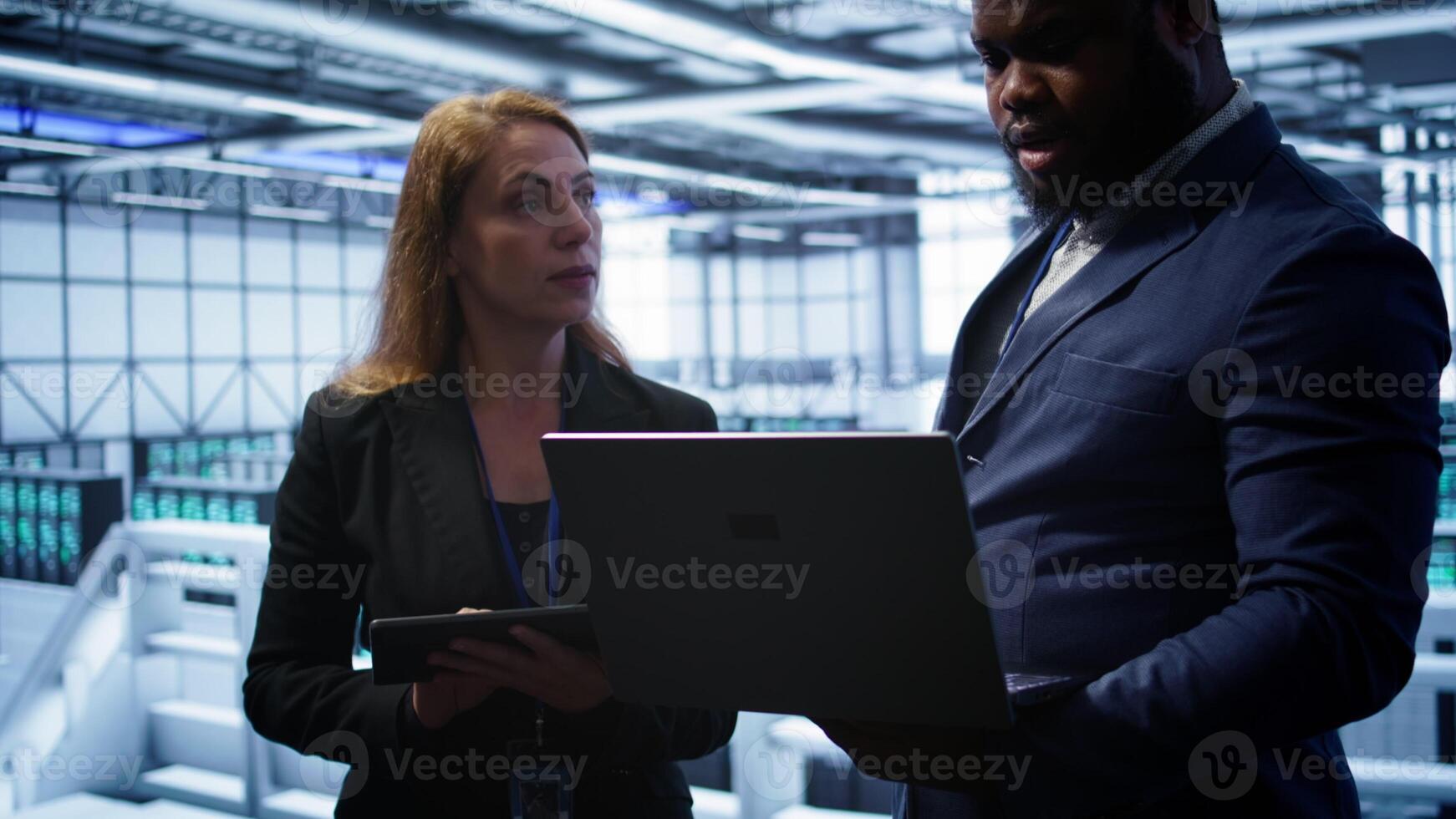 Team of IT specialists managing data center with advanced technology using devices. Coworkers in server room optimizing data center hardware equipment with laptop and tablet, camera B photo