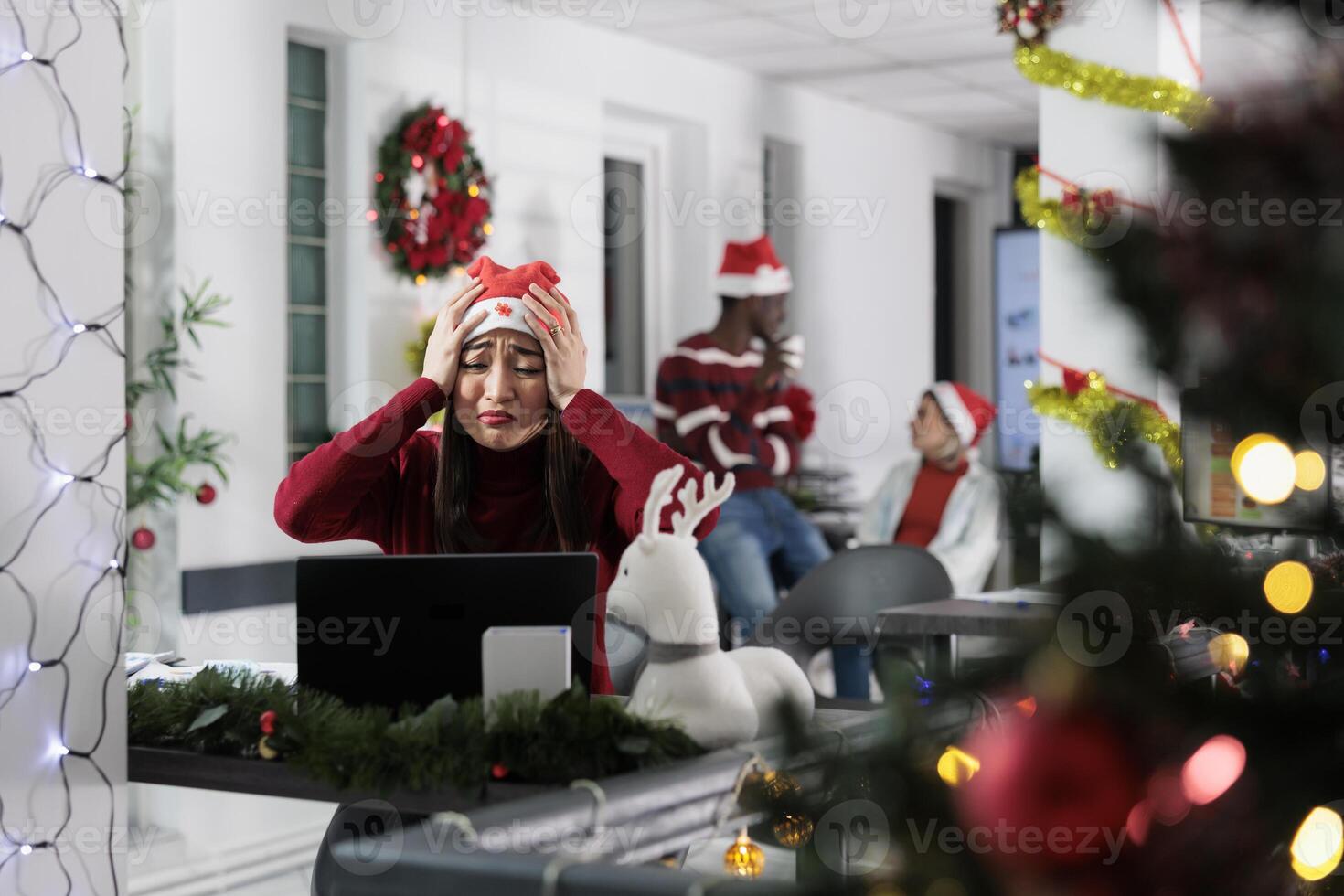 Asian employee in xmas decorated office devastated by bad news email received while at work. Worker in festive ornate workspace finding out her Christmas vacation plans are getting canceled photo