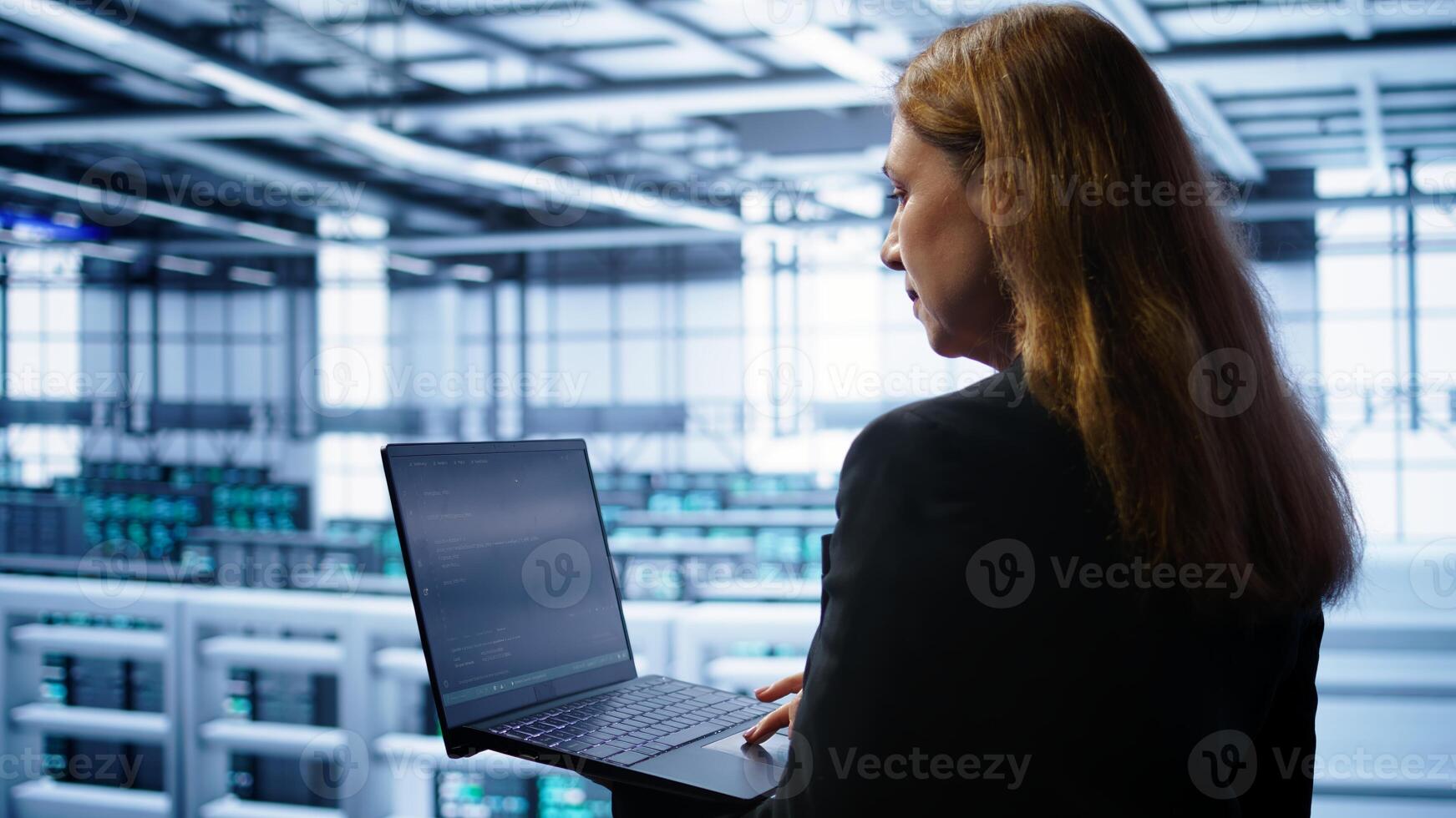 System administrator in data center typing on laptop, running error checking utilities to fix problems. Woman in server hub looking for network issues affecting rigs using notebook device, camera B photo