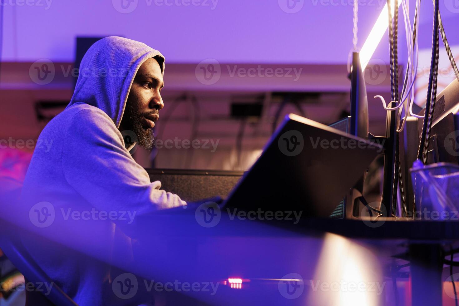 Hacker breaking law while coding illegal ransomware for stealing privacy data. Internet scammer in hood planning online fraud while programming malicious software on computer photo