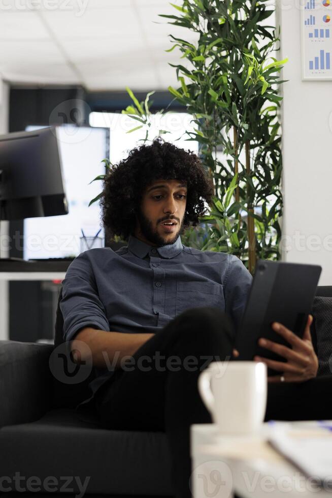 Arab business professional monitoring project analytics on digital tablet. Young company executive manager planning strategy while typing on portable device in start up office photo