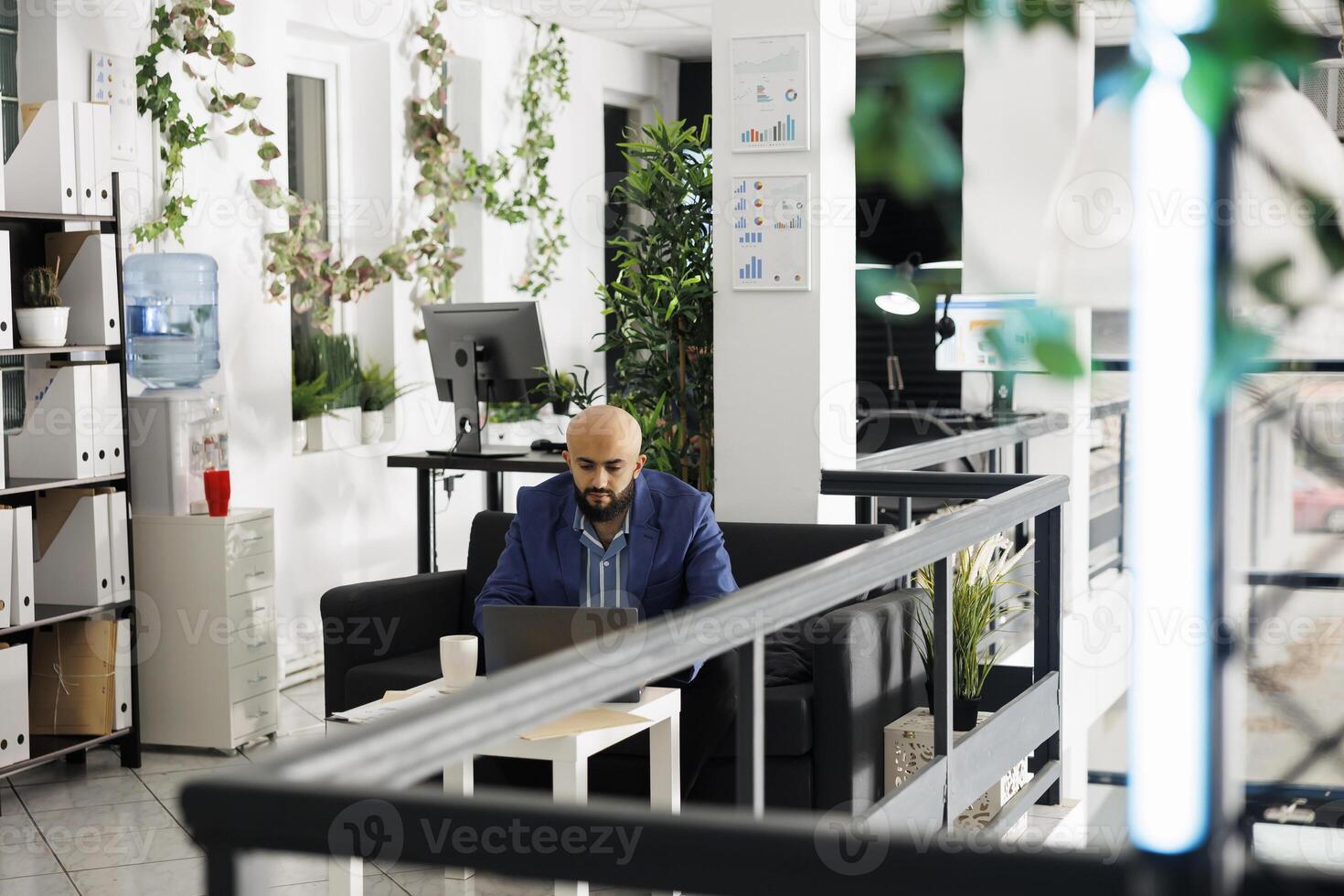 Company arab executive manager analyzing start up strategy on laptop, working in green office. Businessman typing financial report on portable computer in corporate coworking space photo