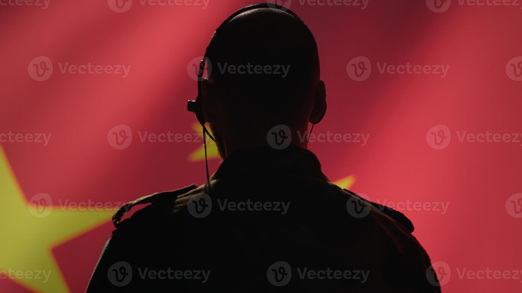 Military dispatcher working for Chinese Communist Party providing informations for troops using headset. Radio communications operator isolated over China flag background coordinating troops, camera A photo