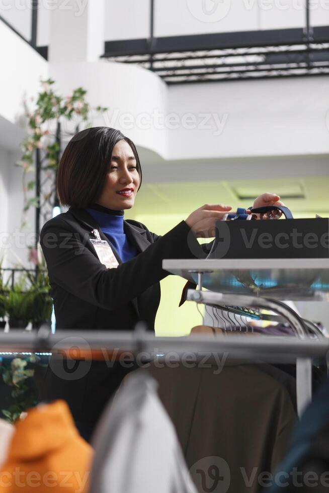 Clothing store smiling woman assistant managing inventory, adjusting trendy accessory on shelf. Seller exploring tie collection while working in department center boutique photo