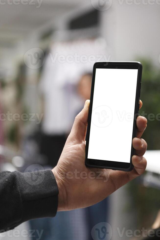 Shopping center boutique customer using smartphone blank digital display and checking sale on online website. Man hand holding mobile phone with empty screen in store closeup photo