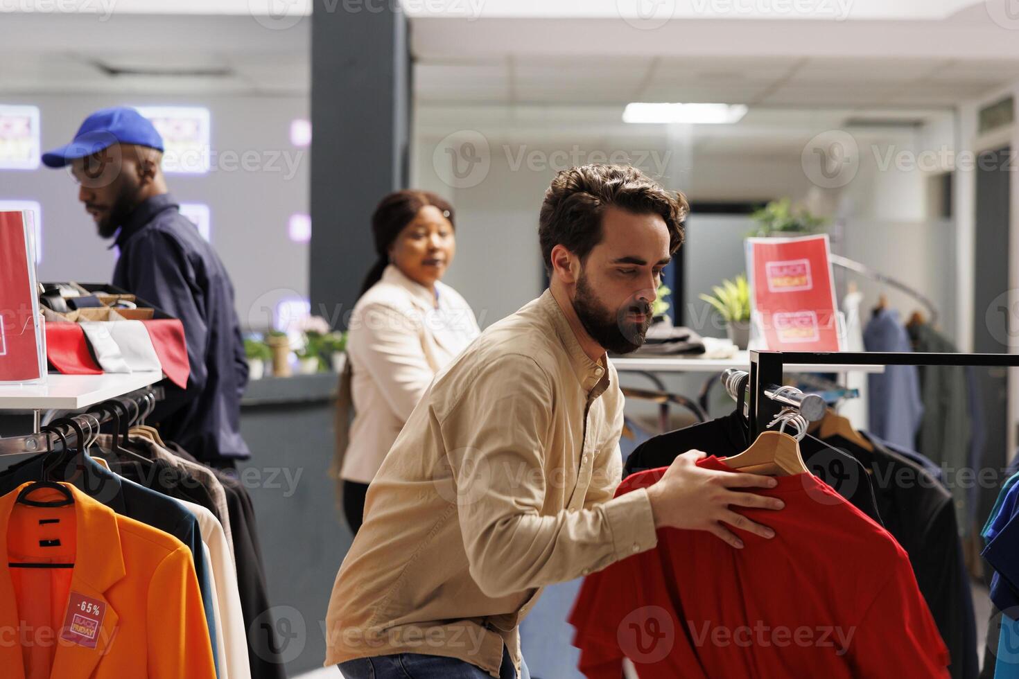 Stressed anxious young guy customer grabbing discounted fashion items while shopping at outlet store, shopaholic man shopper hunting for bargains during seasonal sales. Black Friday and Cyber Monday photo