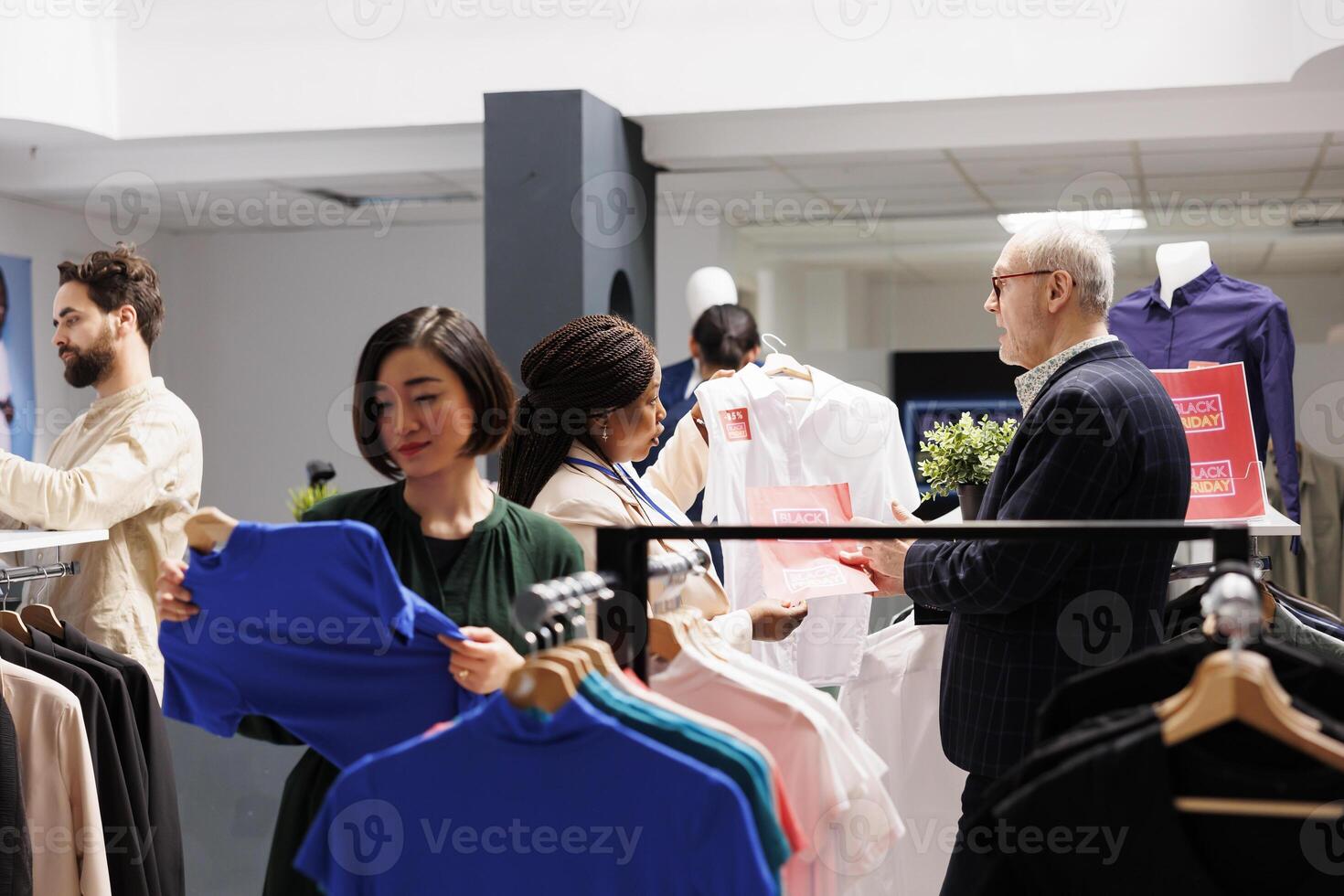 Customer service during Black Friday. Retail worker having conversation with senior man customer in crowded clothing store during seasonal sales, helping shopper to choose clothes at discounted prices photo