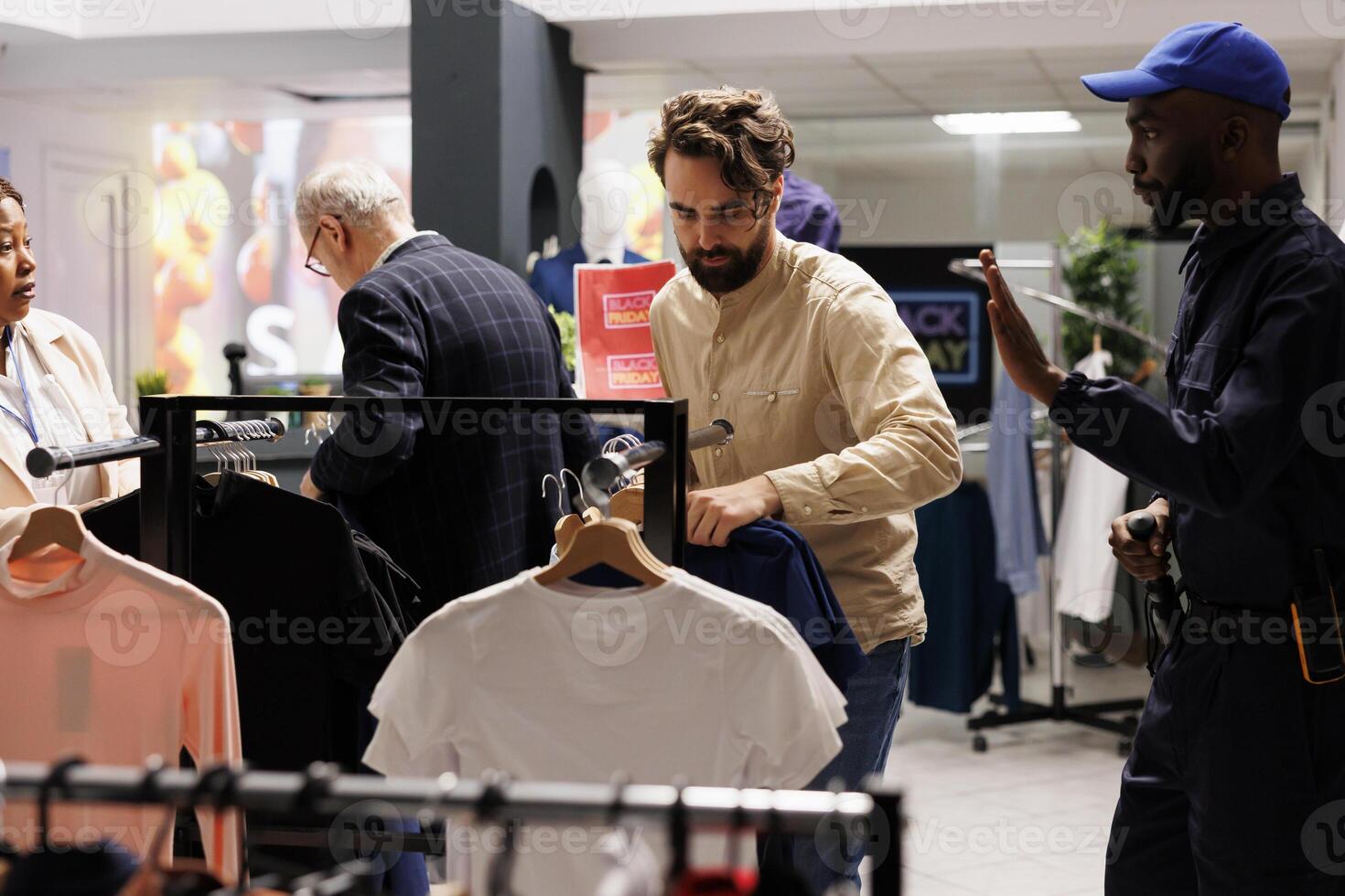 African American guy security guard working in clothing store during Black Friday sales, asking aggressive shopaholic man customer to stay calm, showing stop gesture with hand. Holiday shopping safety photo