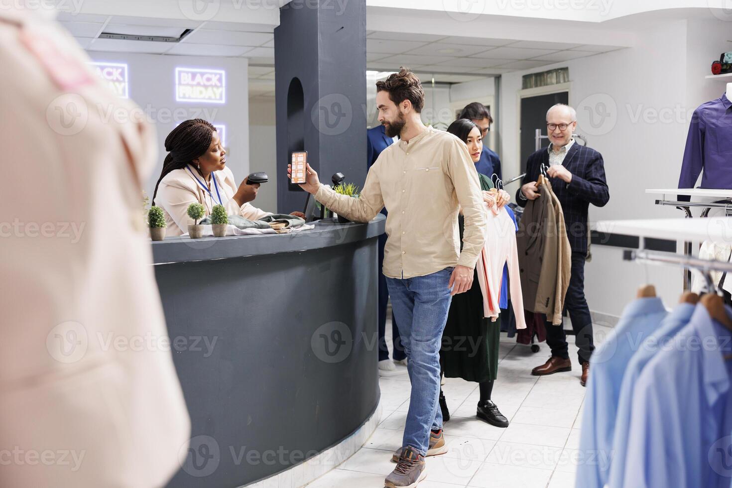 Black Friday shopping. Friendly African American woman clothing store cashier serving male customer, saleswoman standing behind cash register desk and scanning mobile promo code from mobile phone photo