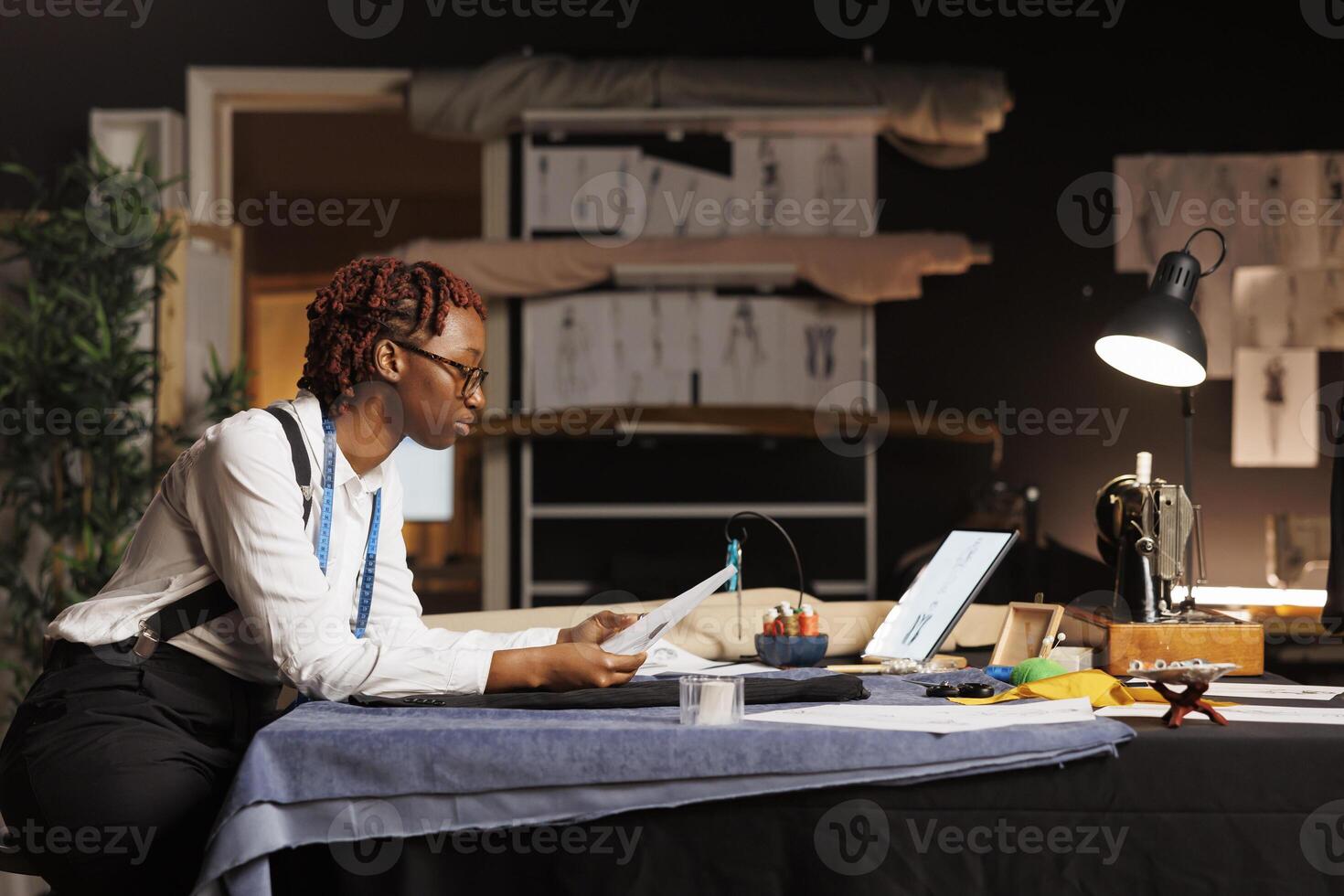 Expert fashion designer looking over bespoken sartorial collection handdrawn sketches. Dressmaker trying to find inspiration in atelier shop workspace before upcoming client comission photo