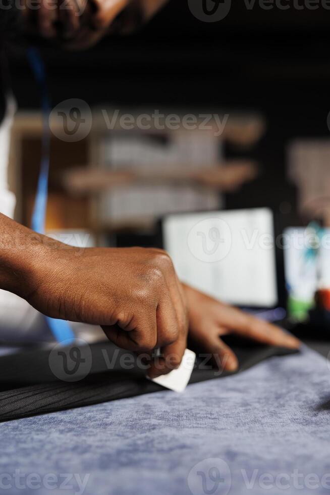 Extreme close up of couturier meticulously checking business suit pants seam in professional atelier studio. Experienced suitmaker finishing comissioned stylish custom made sartorial outfit photo