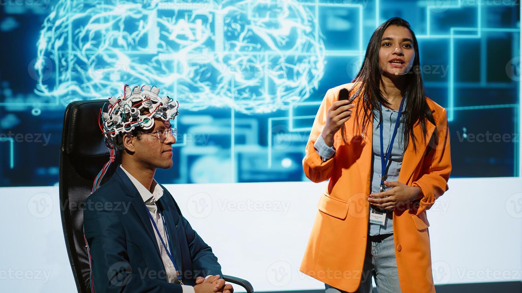 Speaker does EEG headset presentation during tech convention, demonstrating successful implementation of AI in driving forward startup businesses, sharing latest neuroscience discoveries, camera A photo