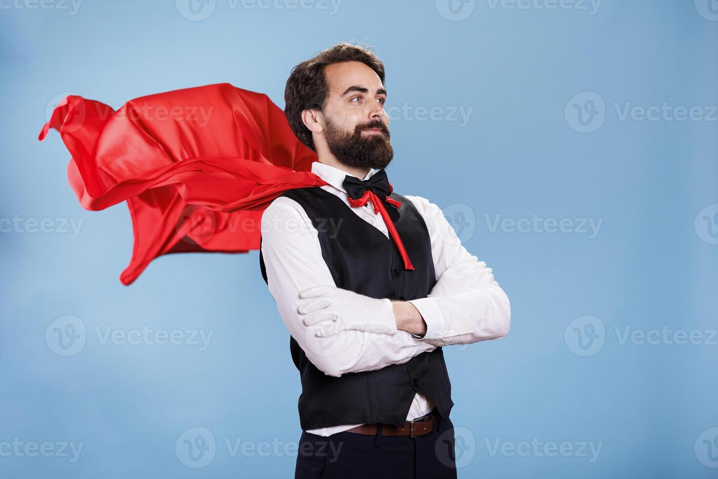 Young man in suit and red cape posing on camera, acting confident as a superhero from cartoon. Powerful determined person wearing red mantle, prepared to save and rescue people. photo