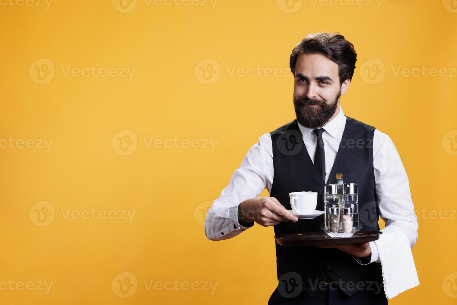 Experienced adult providing coffee cup to customers, acting like a professional butler with suit and tie in restaurant dining industry. Young person serving drinks to clients, formal personnel. photo