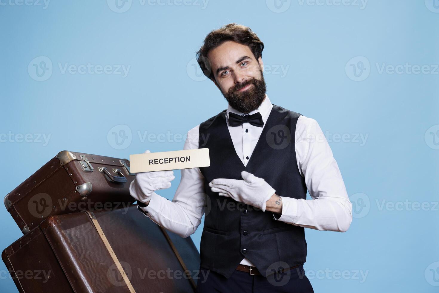 Hotel staff uses reception pointer in studio, guiding guests in the right direction. Stylish doorman employee working in hospitality industry, showing front desk indicator on camera. photo