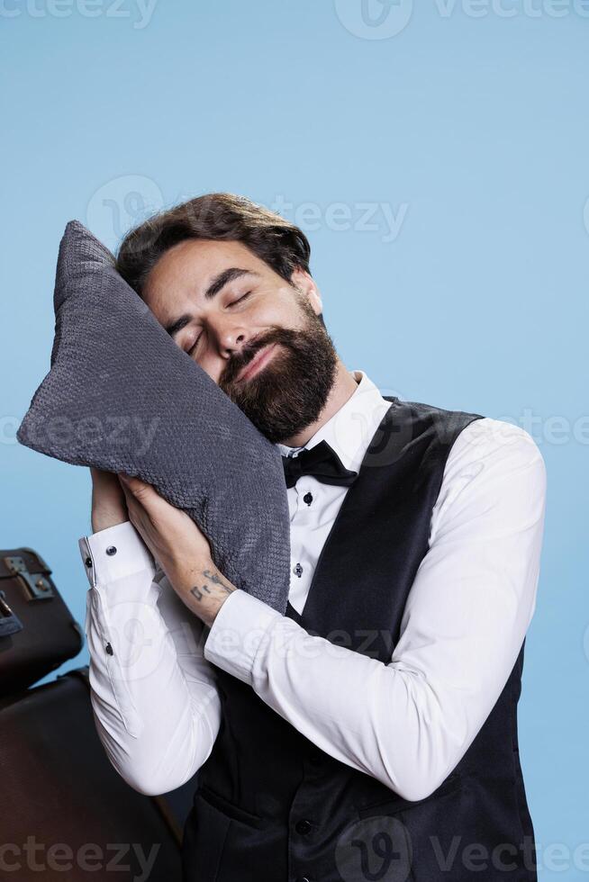 In a sophisticated occupation, hotel employee drifts away over blue background, implying tiredness and weariness. Doorman who had been overworked and worn out took brief snooze or nap. photo
