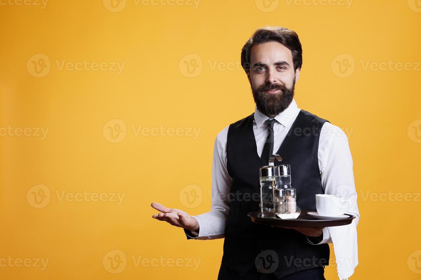 Professional butler serving cup of coffee for clients at restaurant table, carrying drinks on tray for excellent luxury service. Young adult in formal attire acting friendly with customers on camera. photo