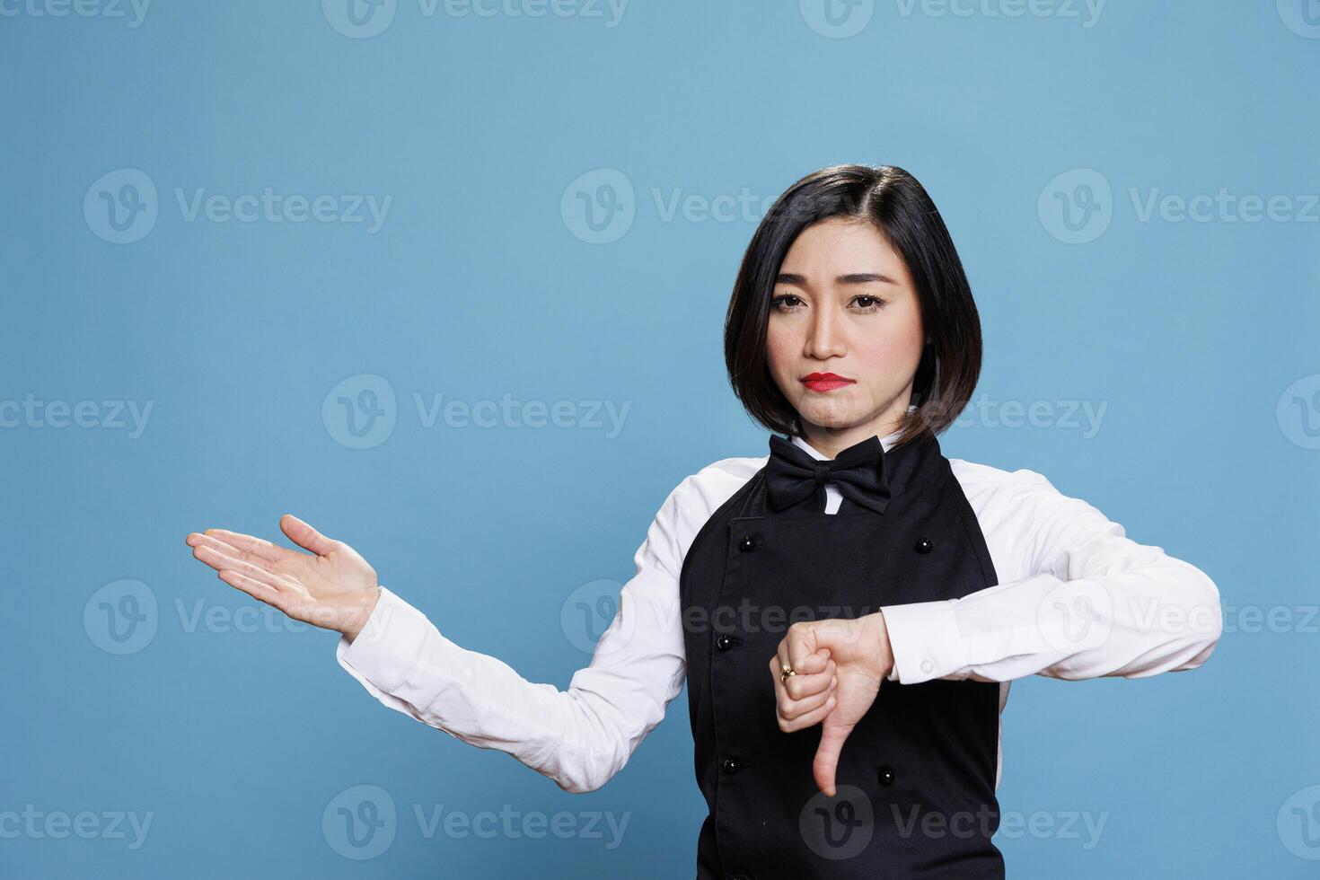 Waitress with thumb down showing negative feedback gesture and pointing to side portrait. Restaurant woman worker displaying disapproval symbol while showcasing to right with hand photo