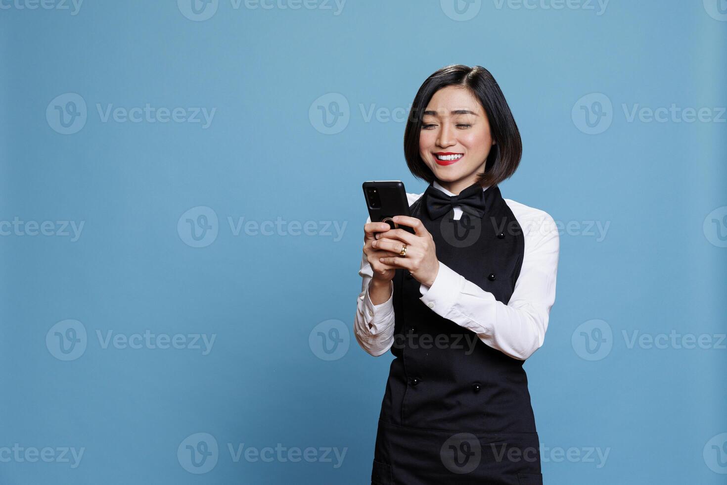 Hotel receptionist holding smartphone and checking message from satisfied customer. Asian waitress with excited face expression reading service positive reviews on mobile phone photo