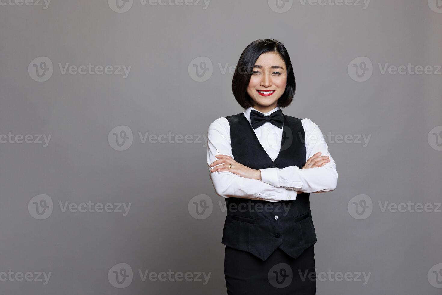 Smiling confident asian woman waitress in uniform standing with crossed arms portrait. Cheerful young professional receptionist posing with folded hands and looking at camera photo
