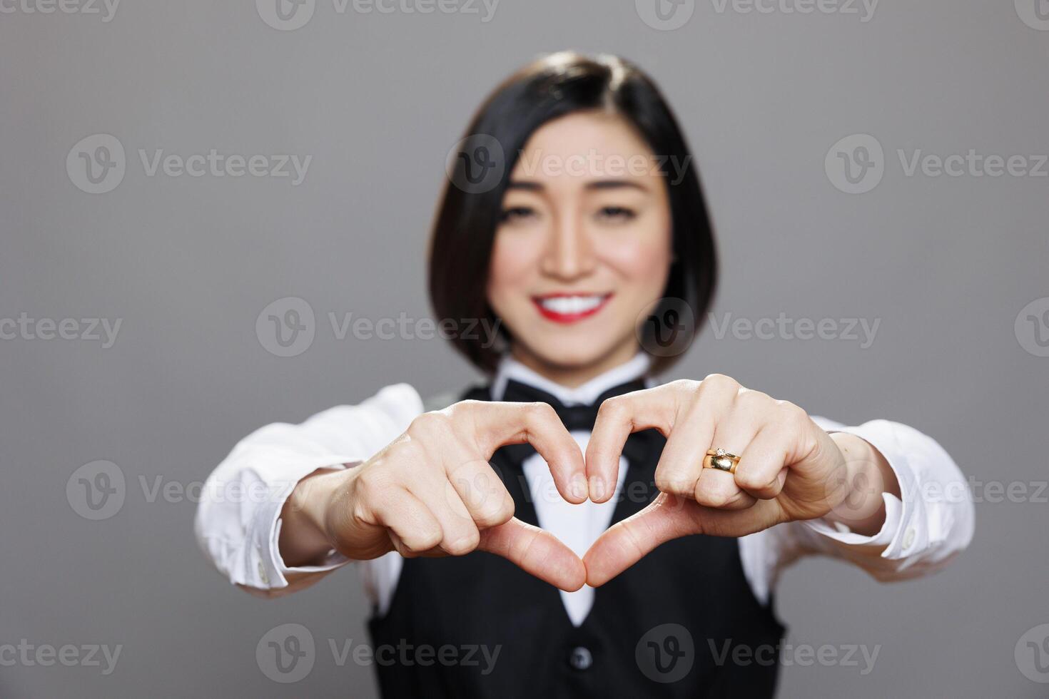 Cheerful asian waitress showing heart sign with fingers, expressing love to restaurant customer portrait. Catering service smiling woman employee showcasing affection symbol photo