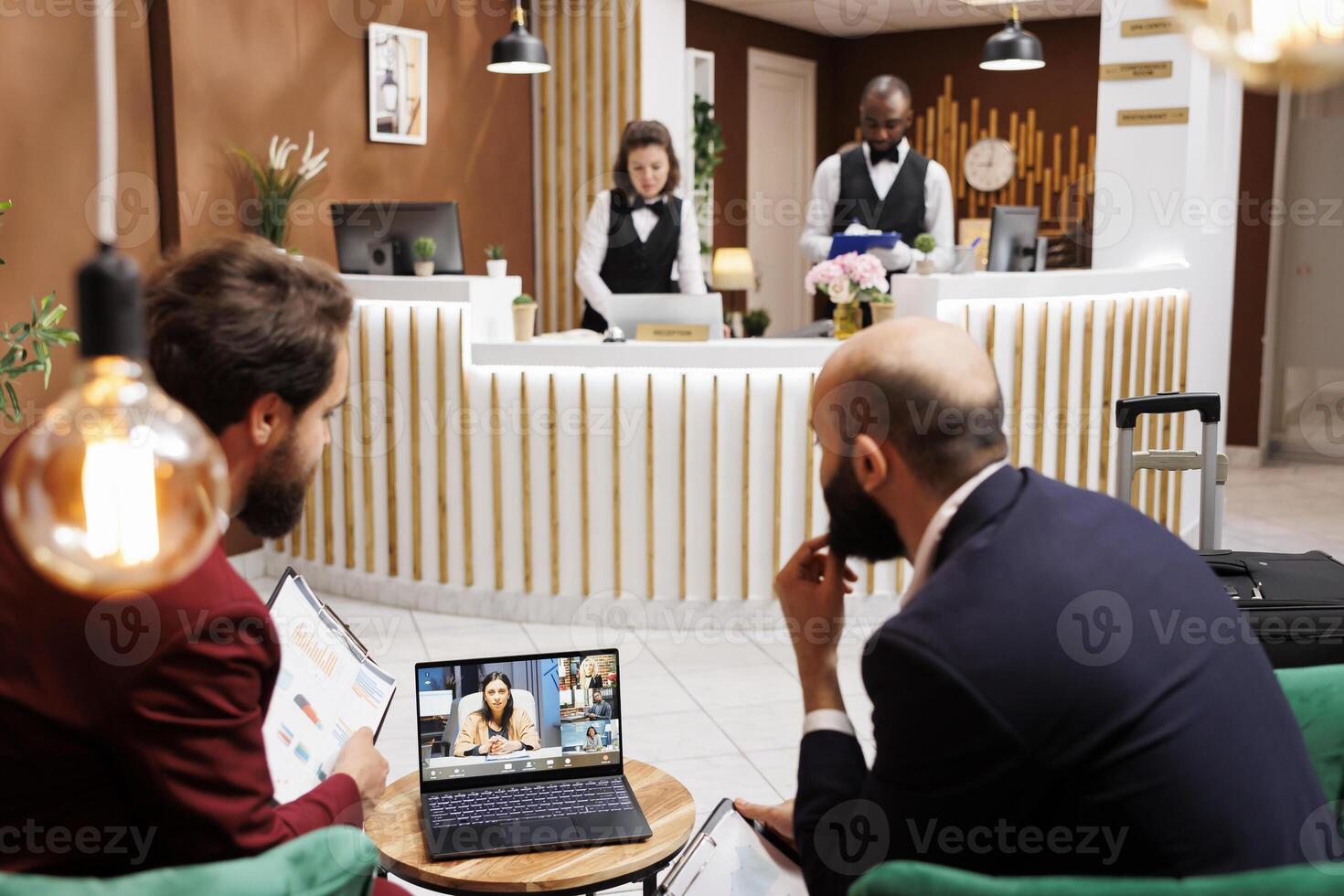 Business professionals on online meeting, using videocall connection to share ideas in hotel reception area. White collar workers attending teleconference and waiting to see accommodation. photo