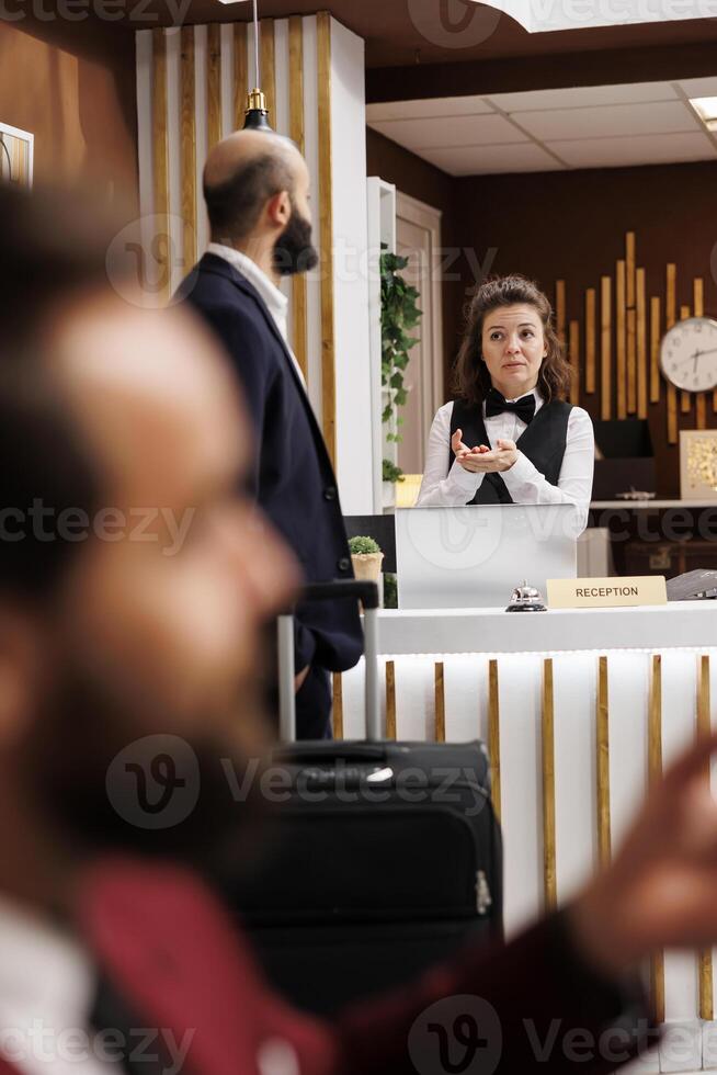 Receptionist greeting business traveller at front desk, sharing tips to ensure relaxing trip apart from meetings. Employee trying to help guest with accommodation, attention to details. photo