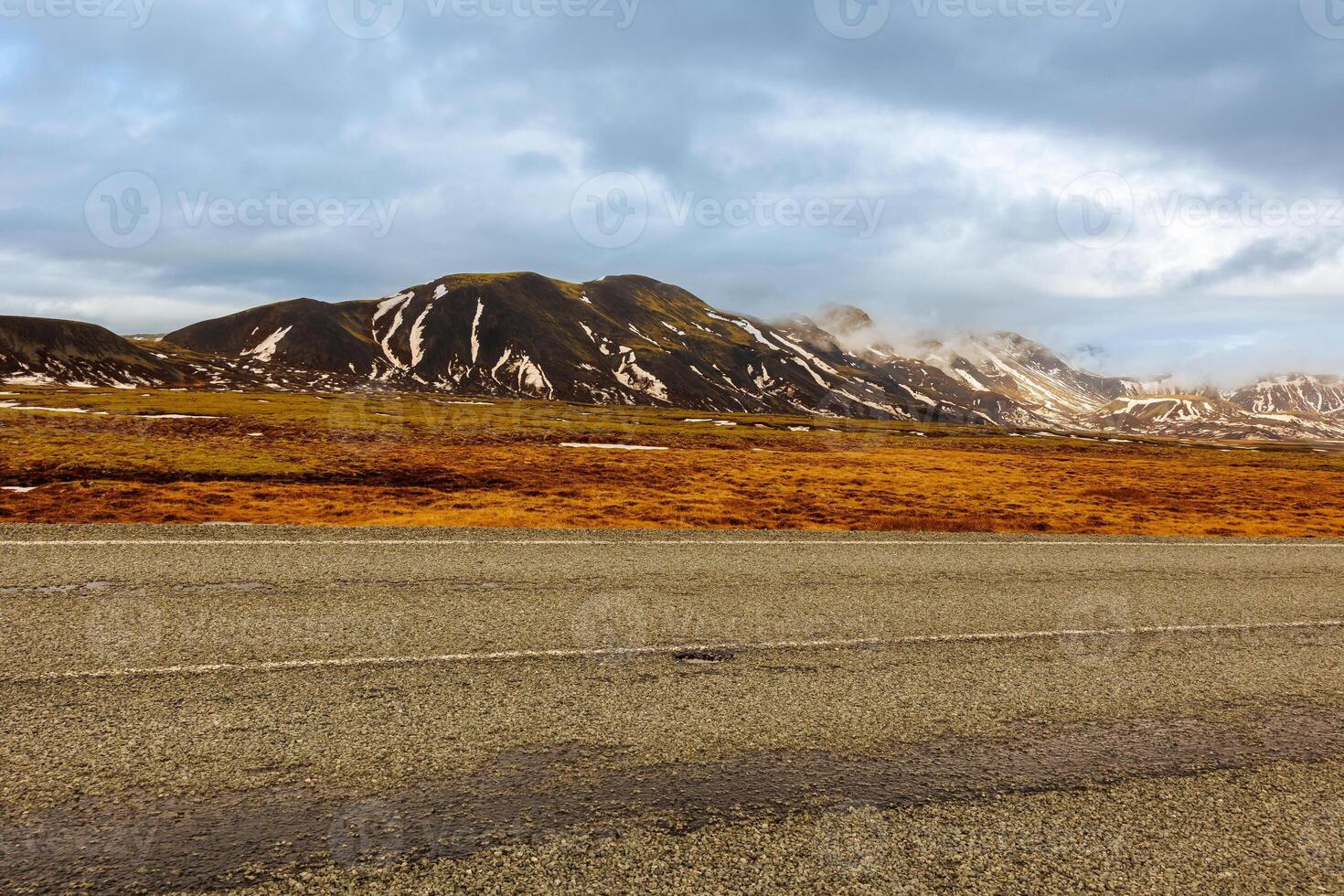 Majestic mountain chain in iceland, lonely road concept near fields and hills in nordic countryside. Beautiful roadside scenery and scandinavian landscapes, massive rocky cliffs with snow. photo