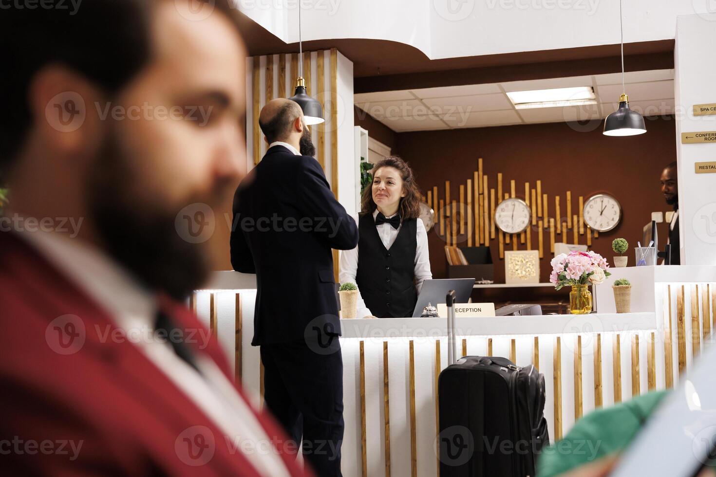 Business traveller arriving at front desk in hotel, talking to receptionist for check in process. Businessman travelling for important meetings abroad, asking for services to ensure pleasant stay. photo