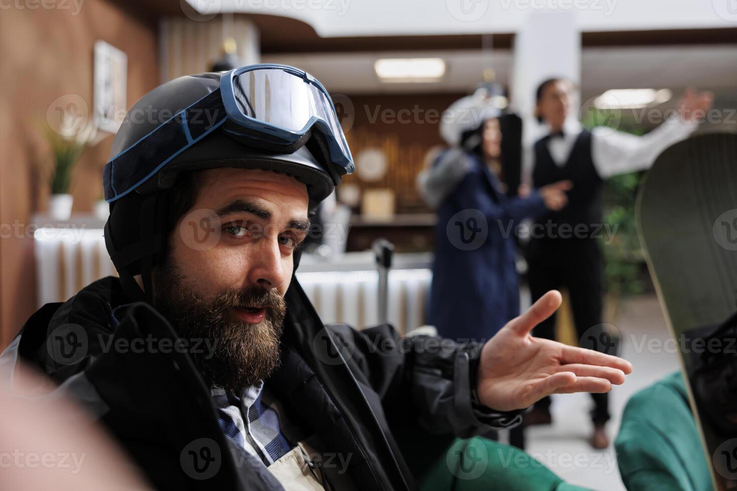 Tourist photographs his journey at ski resort while outfitted in snow gear and holding smartphone. Male guest captures the joy of snowboarding and skiing sports by taking a photo in the hotel foyer.