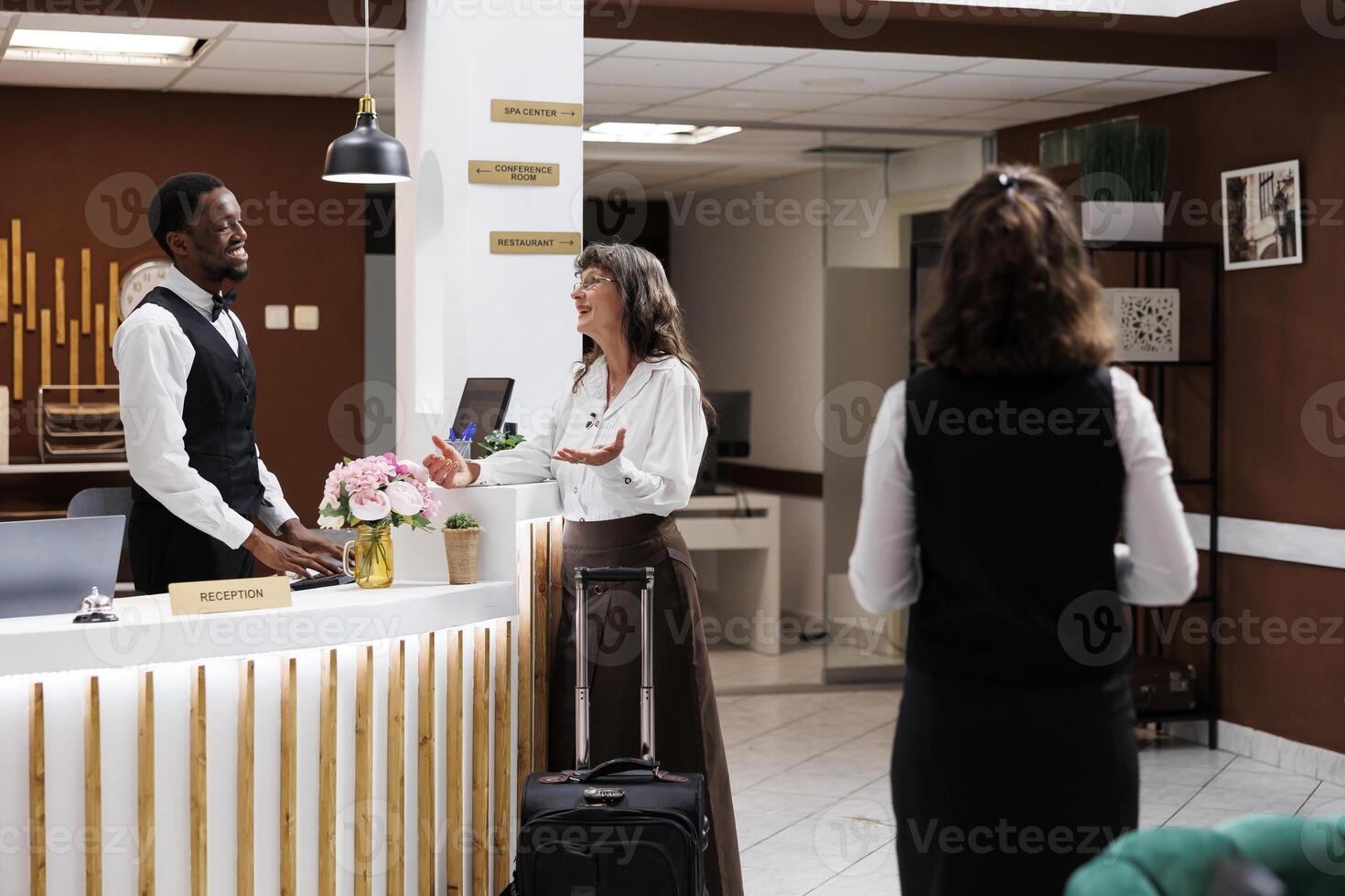 Friendly african american concierge welcomes retired elderly woman and assists with check-in. At luxury resort, senior female tourist speaking with male receptionists about best holiday activities. photo