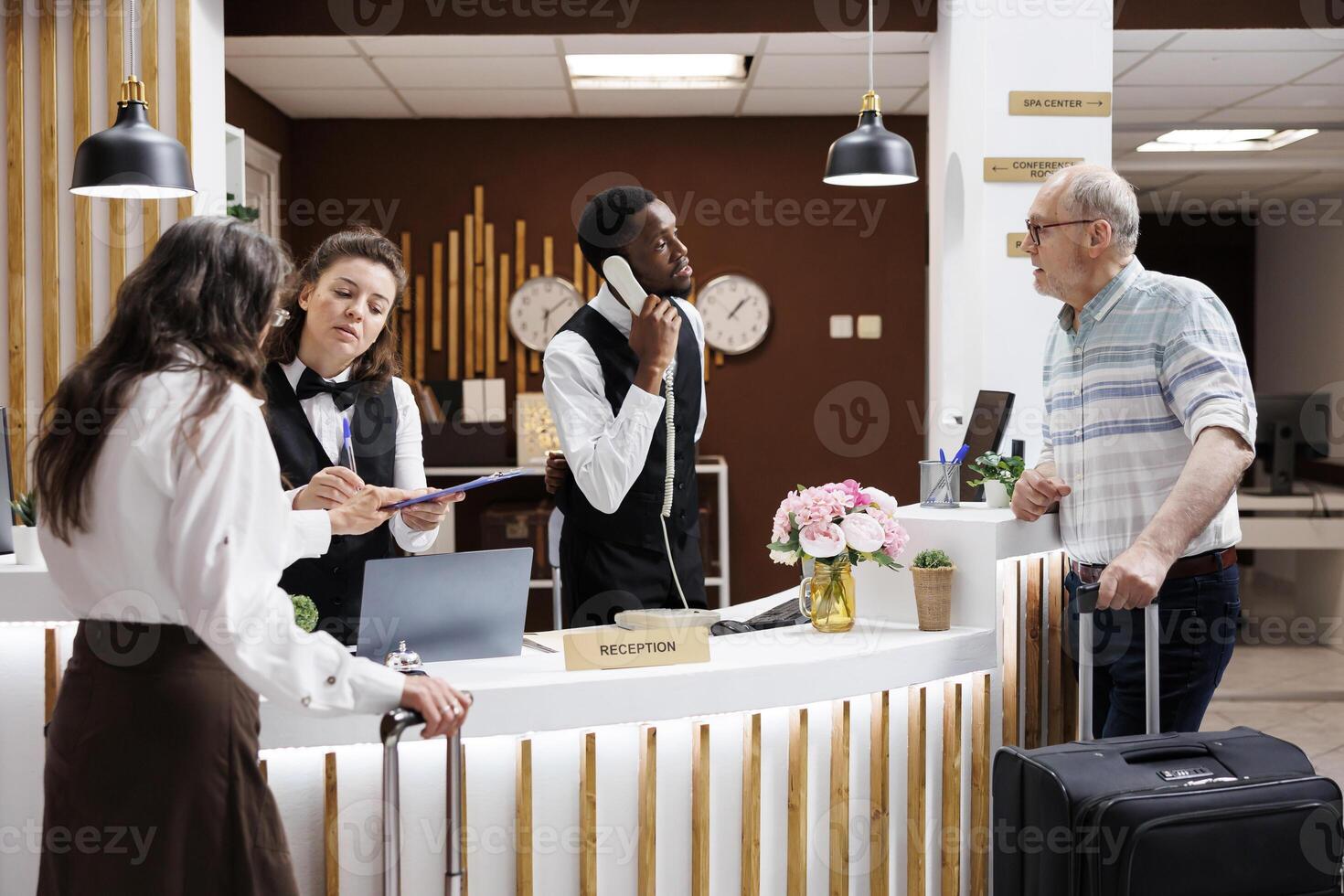 Hotel receptionists assisting elderly travelers with check-in at front desk. Grateful senior woman signs documents with smiles while staff ensures smooth process. Exceptional customer service. photo