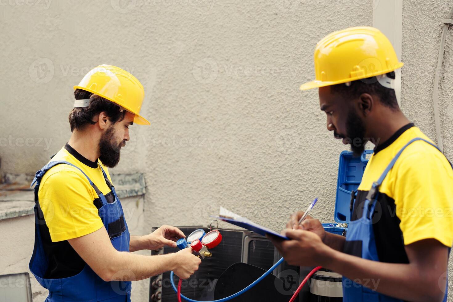Competent mechanic using manifold gauges to read pressure of liquids and gases in hvac system while wireman writes air conditioner inspection and safety check report on clipboard photo