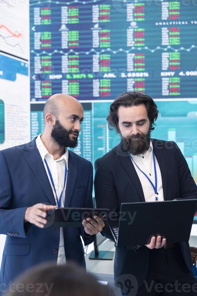 Diverse group of business specialists solve their daily tasks in control room with big screen, analyzing data numbers to ensure organizational progress. Startup management team. photo